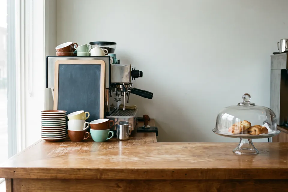The counter of an independent café in the morning, cups stacked beside the espresso machine